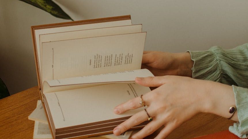 faceless female reading book at table near cup of coffee on saucer