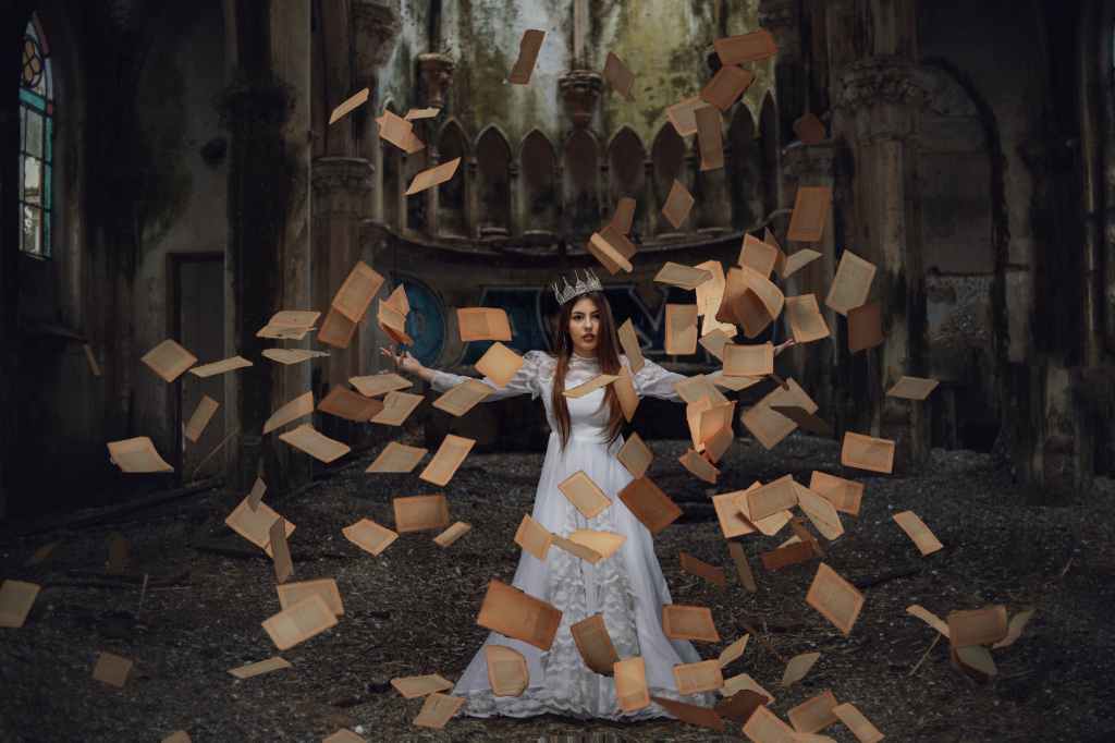 woman in a costume and a crown with old yellow book pages flying around her