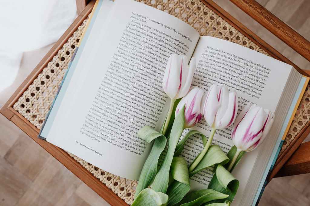composition of fresh romantic flowers on open book arranged on vintage wicker table at home