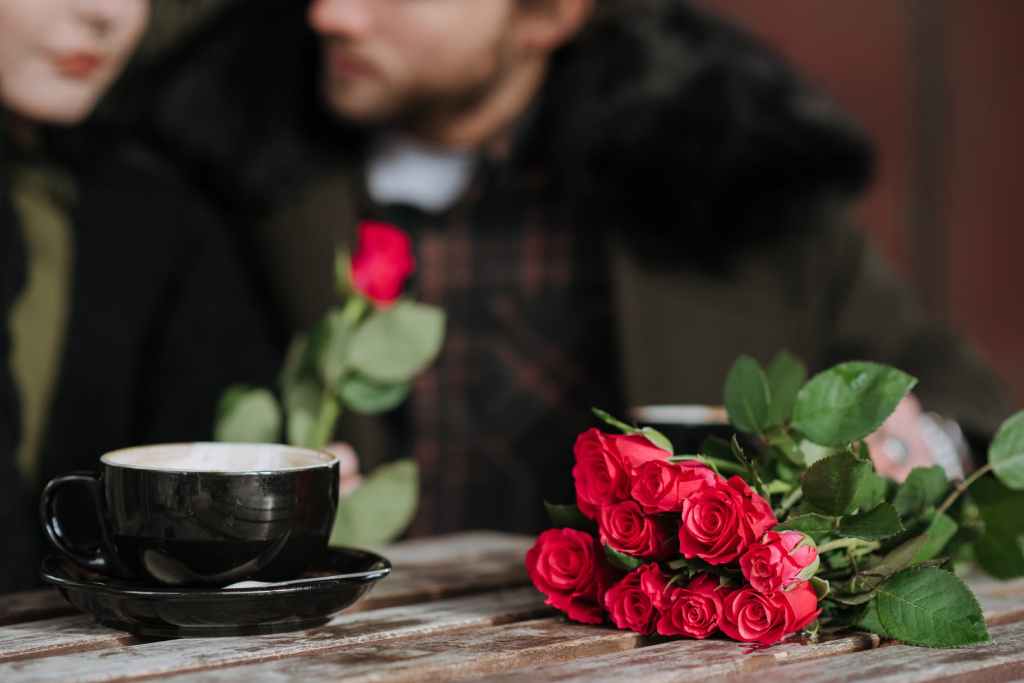 anonymous couple at cafe table with blooming roses and coffee