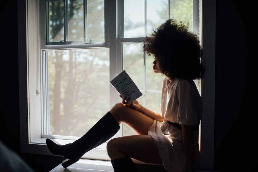 black woman sitting on window reading book