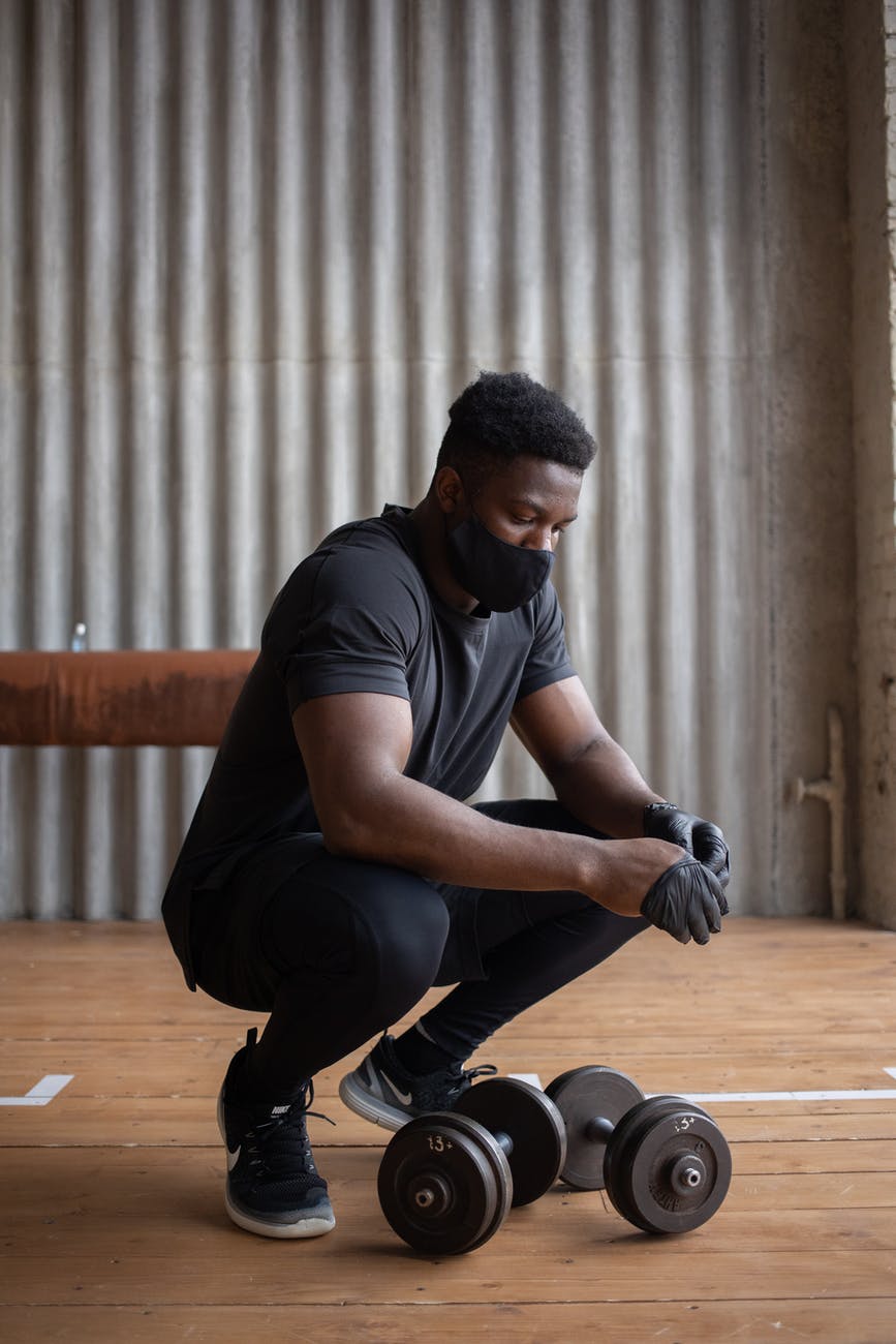 black sportsman in mask putting on gloves near dumbbells; the jock; stock character