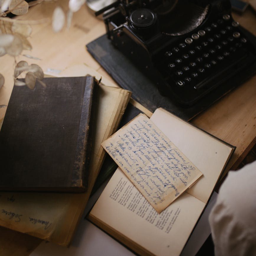 a black typewriter with a bond paper beside a book on a wooden table
