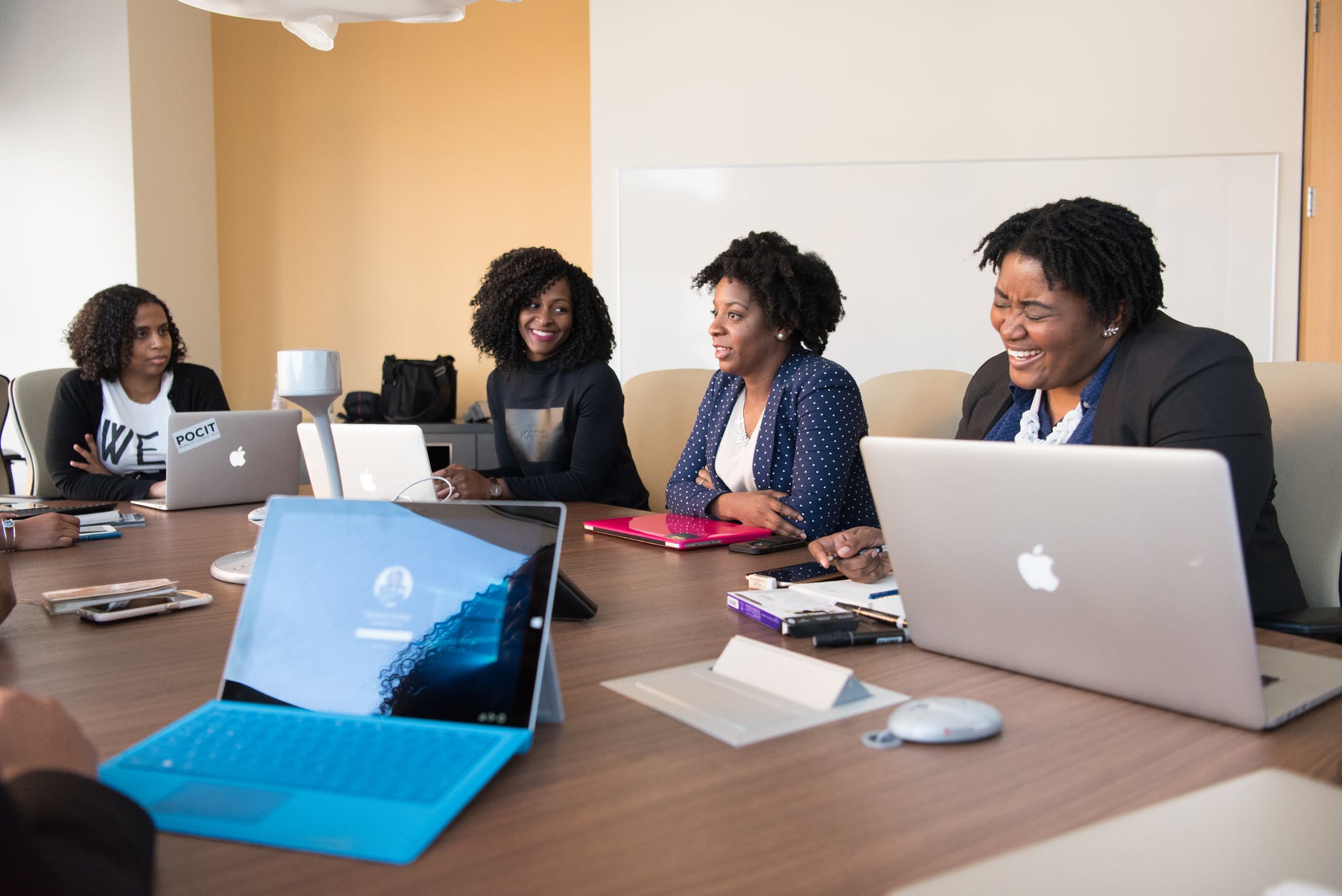 group of black women/ people talking to each other in front of brown wooden table