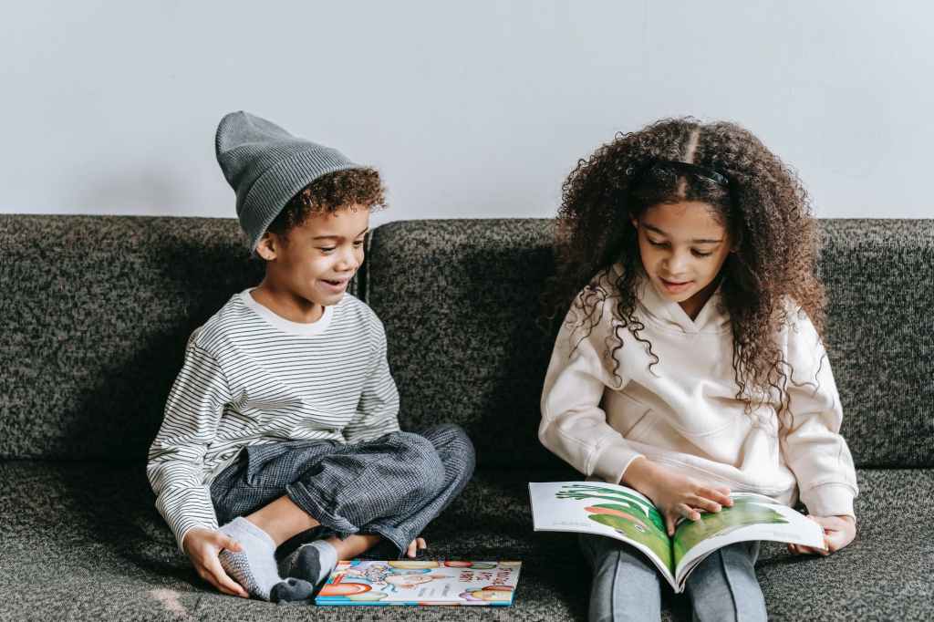 delighted ethnic little siblings reading interesting book on couch