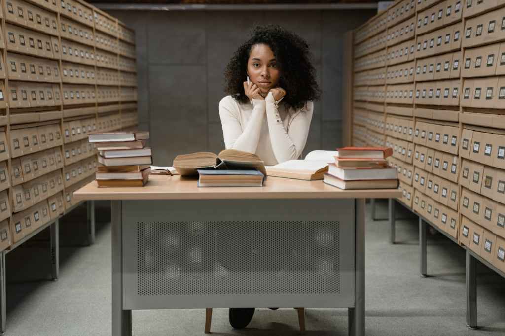 a woman with curly hair sitting on a table with stacks of books