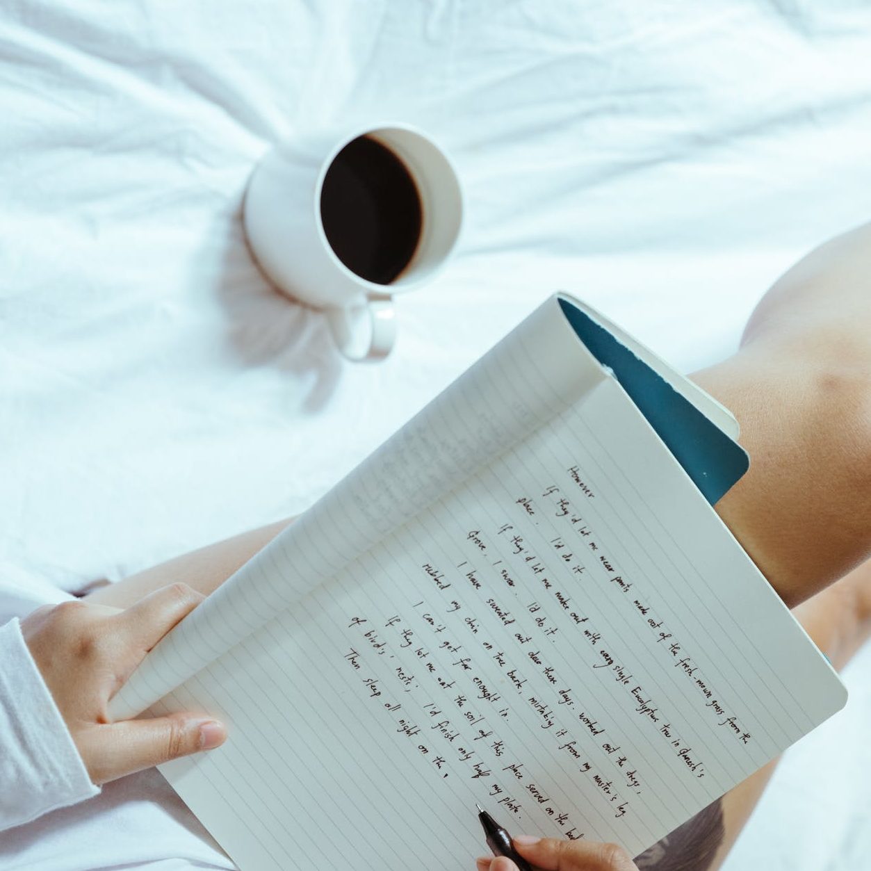 crop woman with coffee writing in notebook on bed