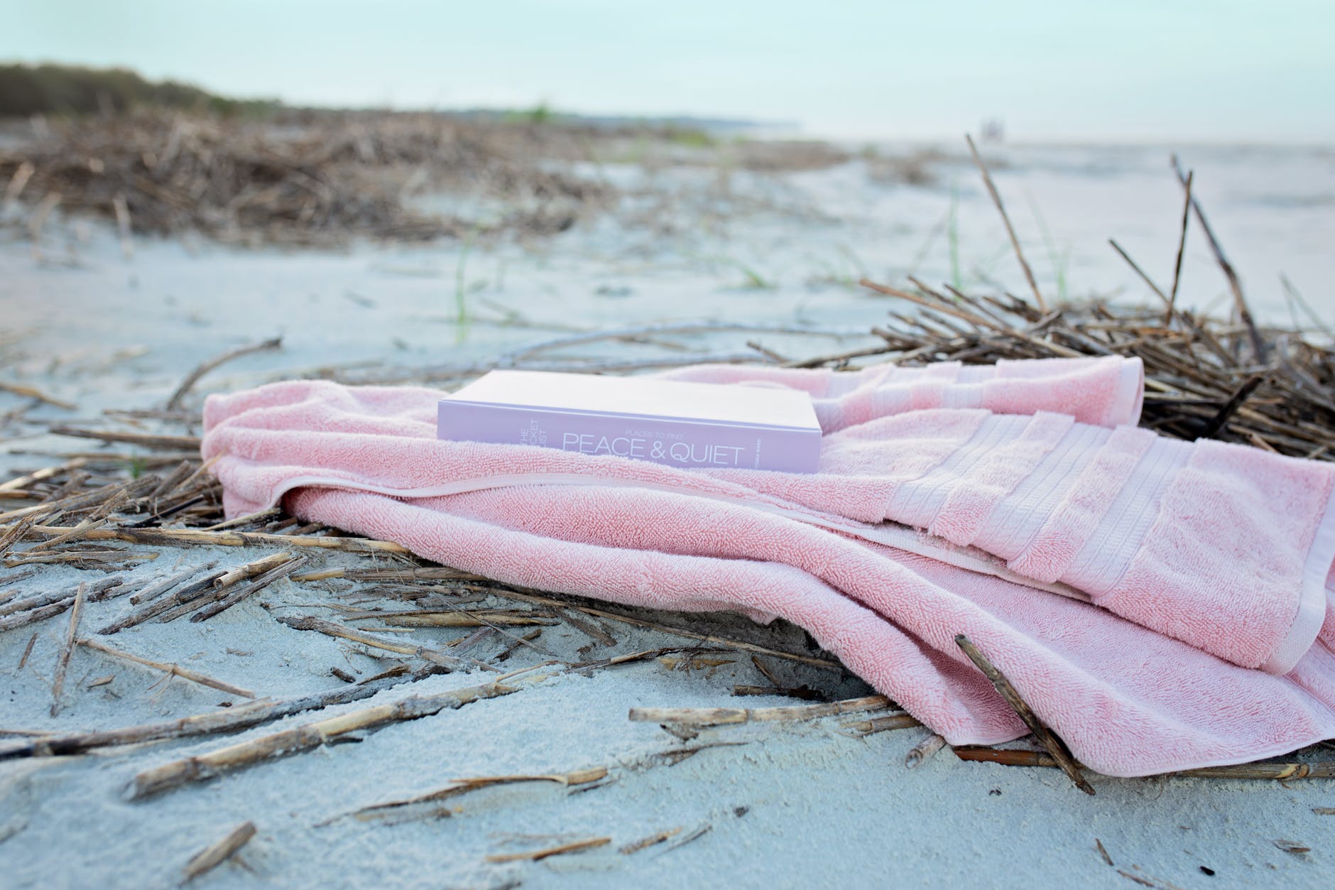 book on pink textile on sand during day;  Castaway Books, interview, Winnifred Tataw