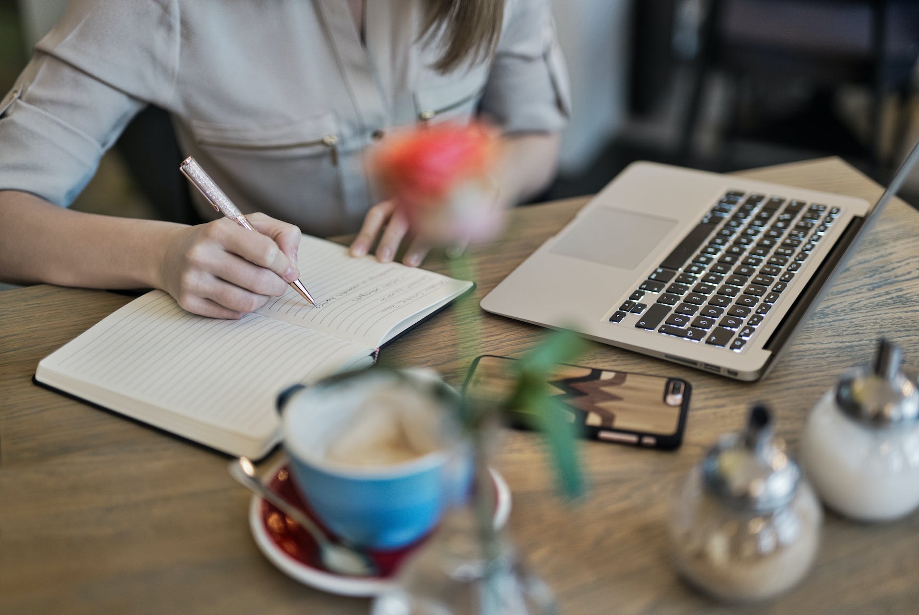 person writing on a notebook beside macbook Photo by Judit Peter on Pexels.com