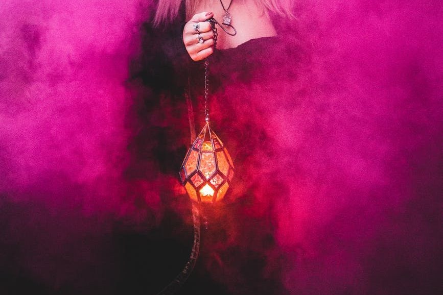 spooky witch with lamp in pink smoke; magic and fantasy